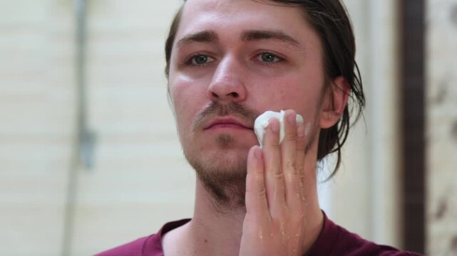 A man applies shaving cream to his face to shave his beard