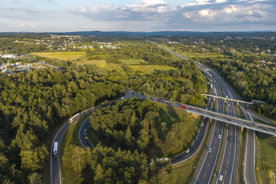 Aerial view of a highway interchange with vehicles driving on the road surrounded by lush green forests and fields in Krakow, Lesser Poland Voivode, Poland.