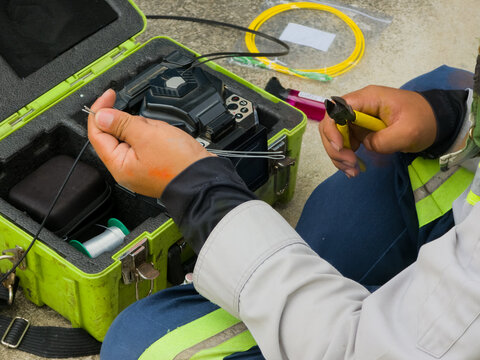 A technician using wire pliers to prepare fiber optic cables next to a fusion splicer machine in a case.