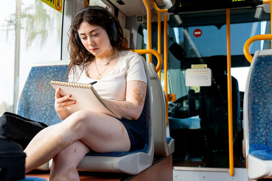 Woman with vitiligo drawing and listening to music on murcia tram, urban commute