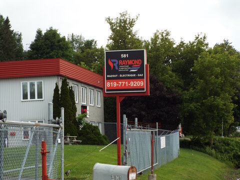 Gatineau, Quebec, Canada &ndash; June 28, 2026: A tall business sign for "Raymond Chauffage Climatisation Ventilation" stands outdoors next to a grey commercial building and fencing at 581 Bd Saint-Ren&eacute; E.