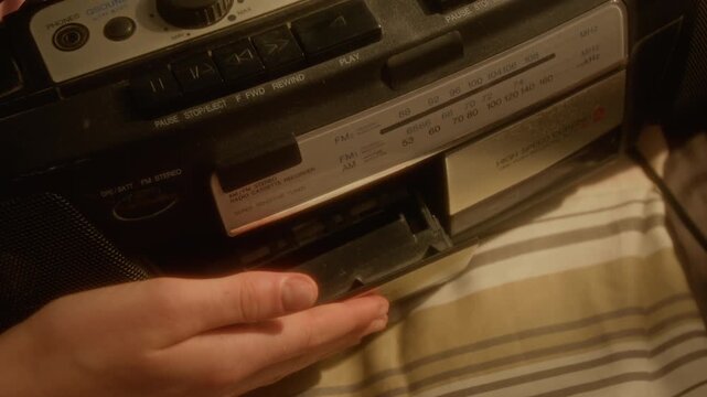 Cropped shot of hand of unrecognizable person opening vintage cassette player, inserting tape, closing deck, and pressing play button. For retro music marketing or nostalgic lifestyle commercials