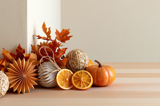 Autumn composition with pumpkins, dried orange slices, colorful leaves and handmade paper ornaments on wooden table with natural copy space