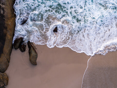 Aerial view of the sandy shoreline and turquoise waves crashing against the rocky outcrops at Lights Beach in Denmark, WA, Australia.