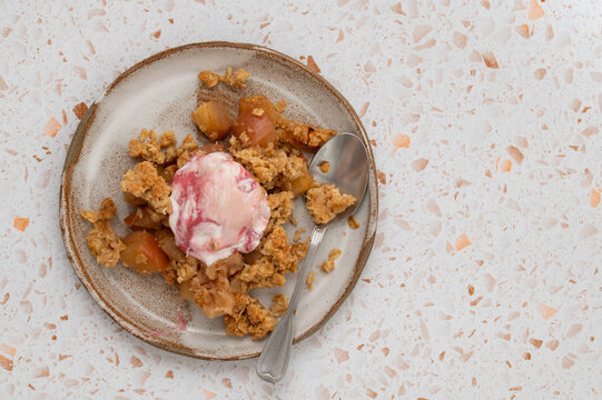 Portion of apple crumble with ice cream and a spoon on a ceramic plate