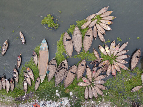 Aerial view of numerous wooden boats arranged in a flower-like pattern on the Buriganga River, surrounded by floating water hyacinths in Dhaka, Bangladesh.