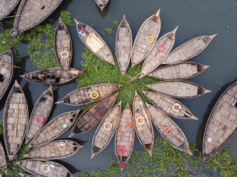 Aerial view of wooden boats arranged in a circular flower-like pattern on the Buriganga River in Dhaka, Bangladesh.