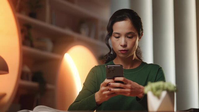 Focused Korean female freelancer types on phone in library, working online