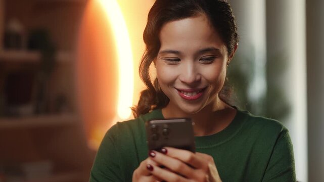 Cheerful Korean female freelancer messages on phone in library, mobile apps