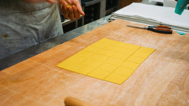 A chef prepares fresh pasta dough, cutting it into small squares for tortelli, a traditional dish from Emilia Romagna
