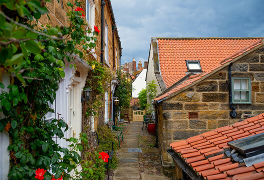 Charming narrow passage between traditional stone cottages with red tiled roofs and climbing roses in Robin Hood&rsquo;s Bay, North Yorkshire, England.
