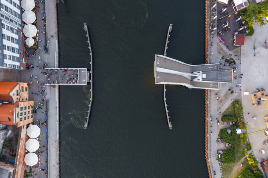 Aerial view of the Footbridge to Olowianka bascule bridge in the open position over the Motlawa River, with historic buildings and people in Gdansk, Pomeranian Voivodeship, Poland.