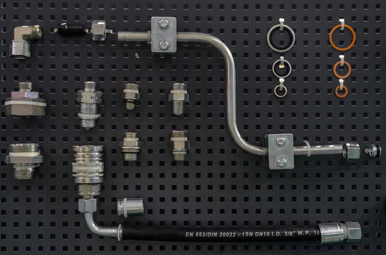 Hydraulic components set with fittings, quick disconnect coupler, bent metal pipe, hose, and rubber O-ring seals on pegboard