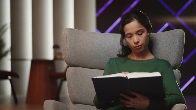Young Korean woman flips through historical book while sitting in armchair