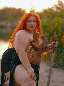 Close-up Plus Size Redhead Warrior Woman Kneeling Holding Sword by Lake