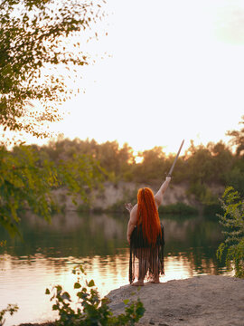 Plus Size Redhead Warrior Woman Raising Sword By Lake Rear View