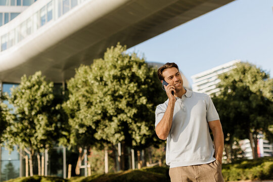 Man talking on the phone under modern architecture in a sunny urban setting
