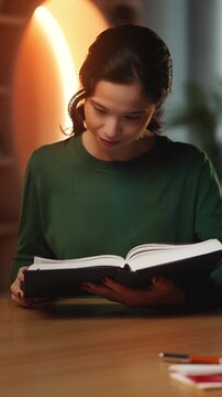 Young Asian woman reads historical book in home study, enjoying her hobby