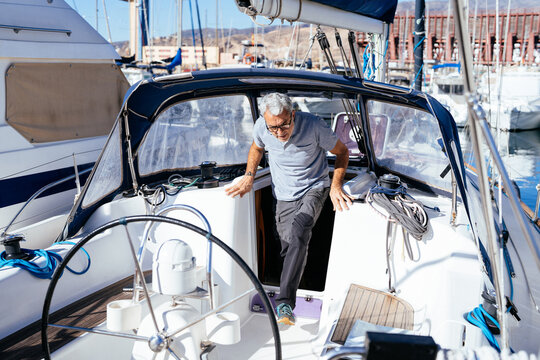 Skilled senior captain walking into helm of cruising yacht at sunrise