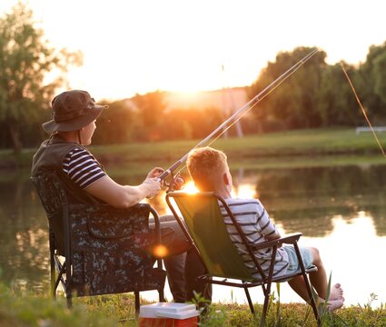 Father and his little son fishing together near river outdoors