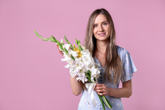Woman with beautiful gladiolus flowers on pink background, space for text