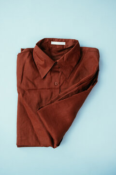 Folded Terracotta Button-Up Shirt on Light Blue Background