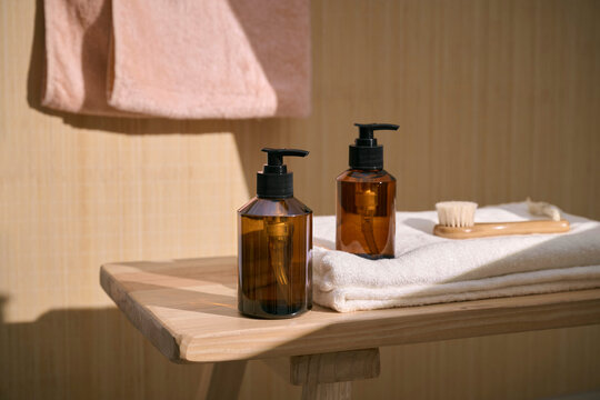 Amber dispenser bottles and facial brush on a wooden shelf