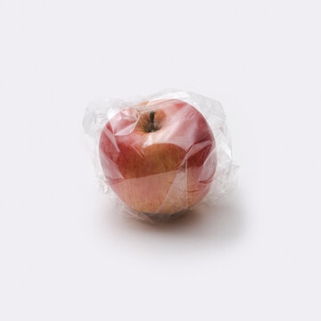 Fresh Red Apple Wrapped in Plastic Foil Representing Plastic Pollution Issue