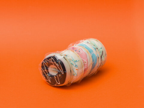 Row of Glazed Donuts Sealed in Plastic Packaging on Orange Surface
