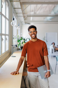 Man smiling, holding laptop in modern workplace