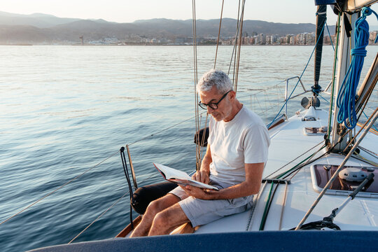 Senior man relaxing reading book on sailboat