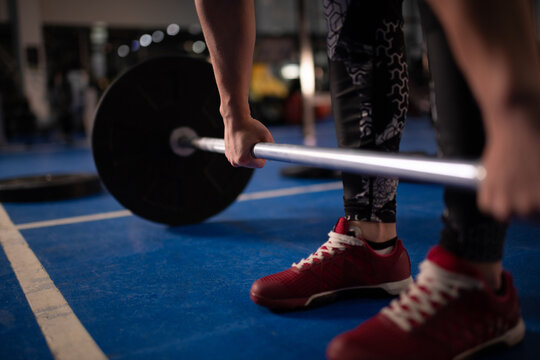 Cropped female athlete deadlifting barbell in gym