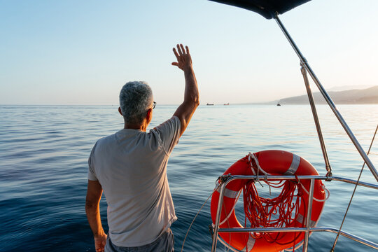 Senior man waving goodbye from sailboat enjoying journey