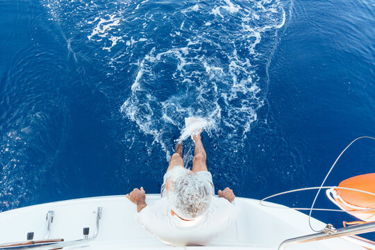 Senior man splashing feet in blue sea from yacht