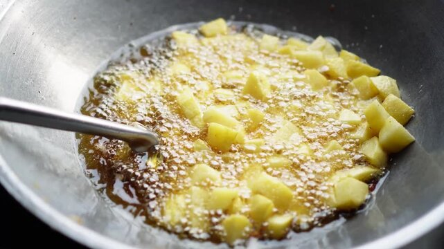 Golden potato cubes frying vigorously in bubbling oil within a metal wok, captured from an overhead angle with a utensil resting inside. Ideal for culinary content or food preparation themes.
