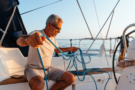 Senior man coiling rope on sailing boat deck