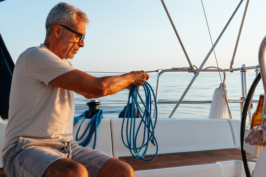 Mature man coiling nautical rope on sailing yacht