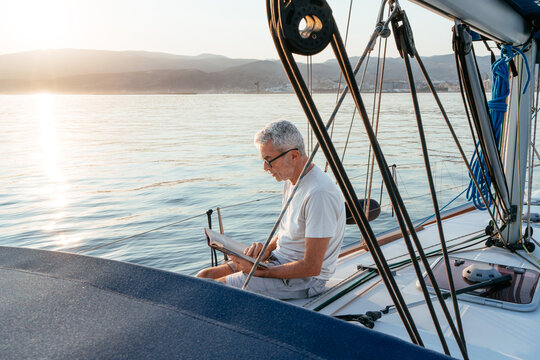 Senior man reading book on sailing yacht at sunset