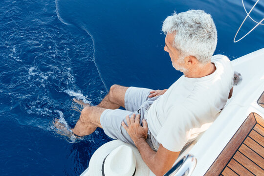 Senior man dangling feet in ocean from sailboat