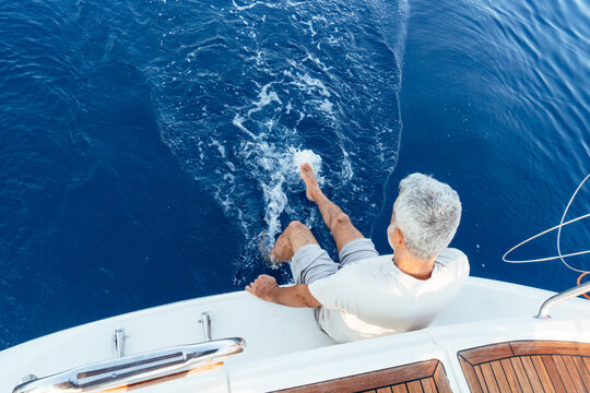 Senior man splashing feet in ocean from sailboat