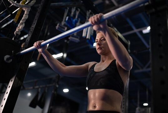 Exhausted female athlete taking barbell from rack