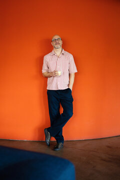 Relaxed Man Holding Coffee Against Orange Wall