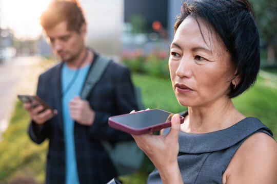 Woman talks into smartphone while man stands in background.