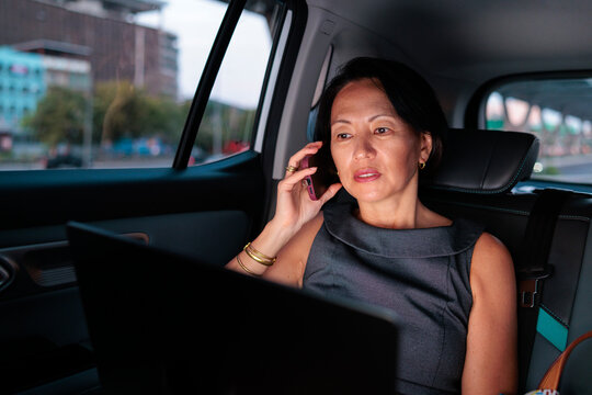 Businesswoman multitasking on a phone and laptop while commuting