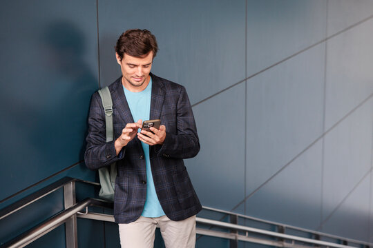 Man in blazer checks smartphone while leaning against wall