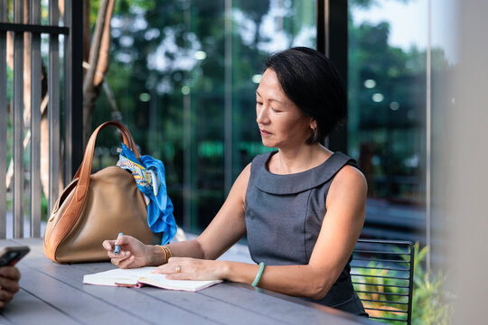 A professional woman writes in a notebook outdoors.