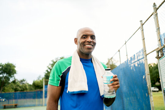 Smiling athletic man hydrating on the court