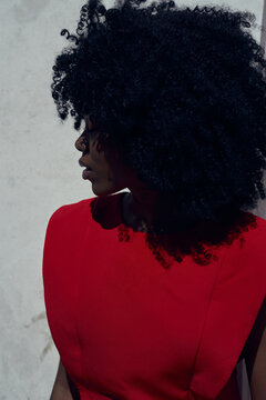 Black fashion woman in red outfit with curly hair stands by wall