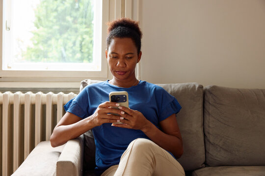Woman rests on a couch, texting on her phone