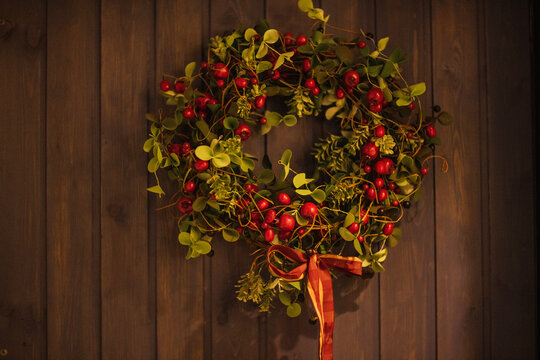 Decorative holiday wreath made of green leaves and red berries with a ribbon bow, hanging on a wooden wall, perfect for seasonal home decor